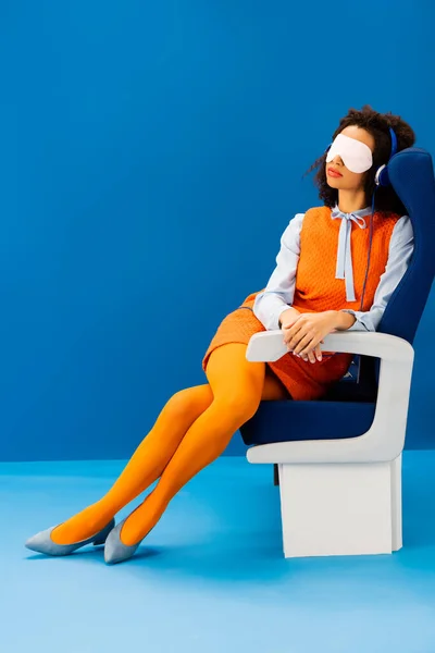 African american with sleeping mask listening to music and sleeping in seat on blue background — Stock Photo