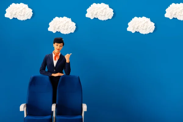 Усміхнений афроамериканський стюардеса, що показує як біля сидіння на синьому фоні з хмарами — стокове фото