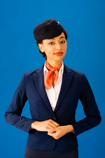 Sorridente assistente di volo afro-americana guardando la telecamera isolata sul blu — Foto stock