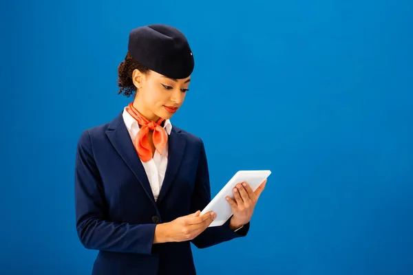 Asistente de vuelo afroamericano sonriente usando tableta digital aislada en azul - foto de stock