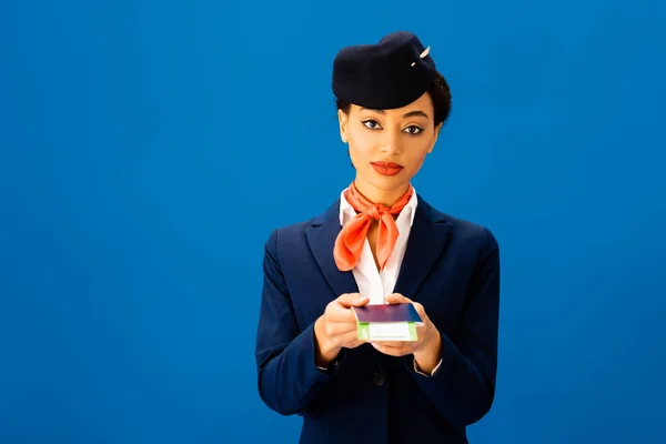 Auxiliar de vuelo afroamericano con pasaporte y billete de avión aislado en azul - foto de stock
