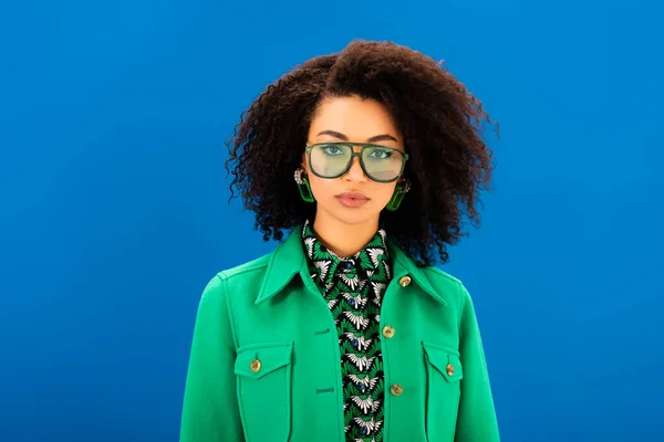 Mujer afroamericana con estilo en la chaqueta mirando a la cámara aislada en azul - foto de stock