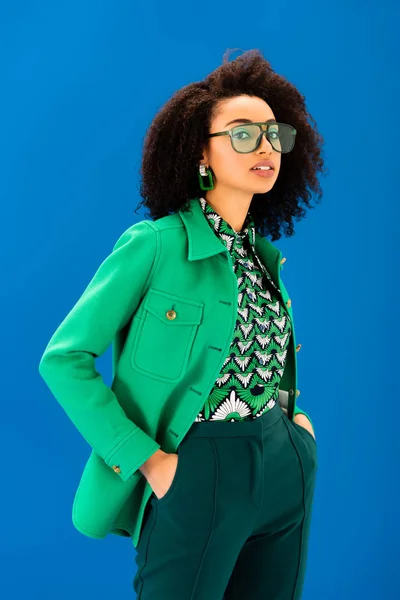 Elegante donna afroamericana con le mani in tasca guardando la fotocamera isolata sul blu — Foto stock