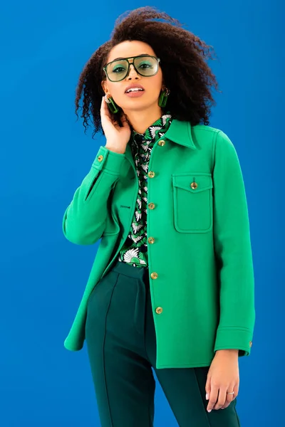 Stylish african american woman in jacket looking at camera isolated on blue — Stock Photo