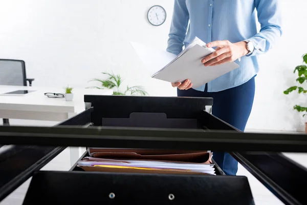 Cropped view of businesswoman holding folder with dossier near open cabinet driver in office — Stock Photo