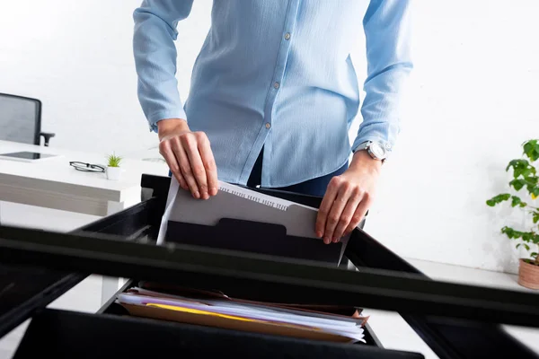 Cropped view of businesswoman taking folder with dossier from open cabinet driver in office — Stock Photo