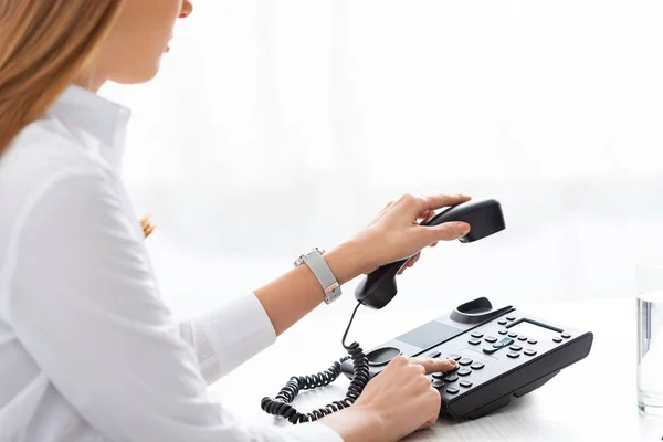 Ausgeschnittene Ansicht einer Geschäftsfrau, die ihr Mobiltelefon hält, während sie das Telefon am Tisch benutzt — Stockfoto