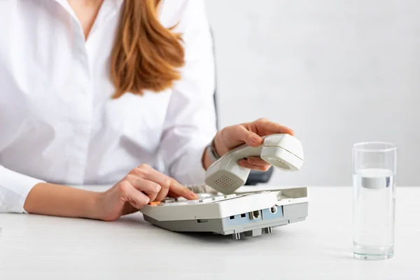 Cropped view of businesswoman using telephone near glass of water on table — Stock Photo