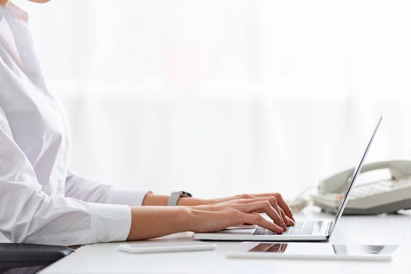 Cropped view of businesswoman using laptop near gadgets on table — Stock Photo