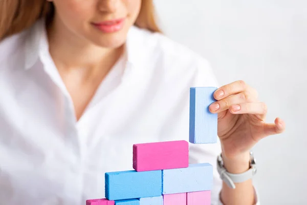 Селективный фокус деловой женщины, укладывающей красочные строительные блоки, изолированные на сером — стоковое фото