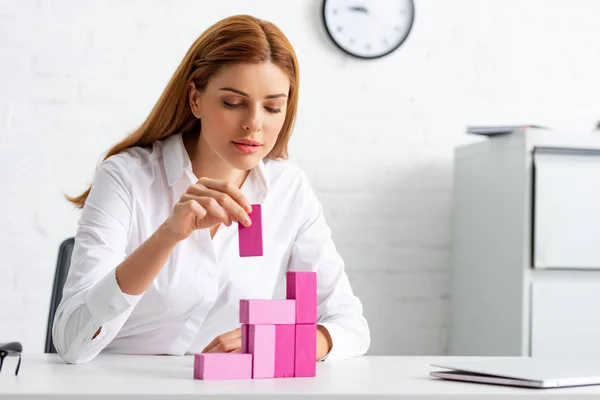 Empresária atraente jogando blocos de construção rosa na mesa — Fotografia de Stock