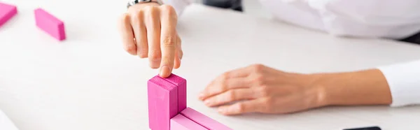 Vista recortada de la mujer de negocios apilando bloques de construcción de color rosa en la mesa, plano panorámico - foto de stock