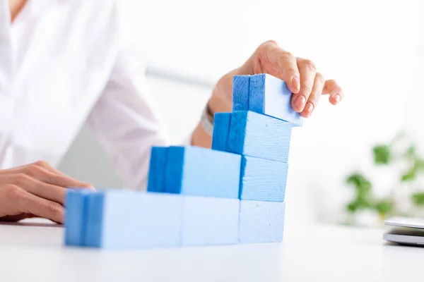 Enfoque selectivo de la mujer de negocios haciendo pirámide de marketing con bloques de construcción azules cerca de la computadora portátil en la mesa - foto de stock