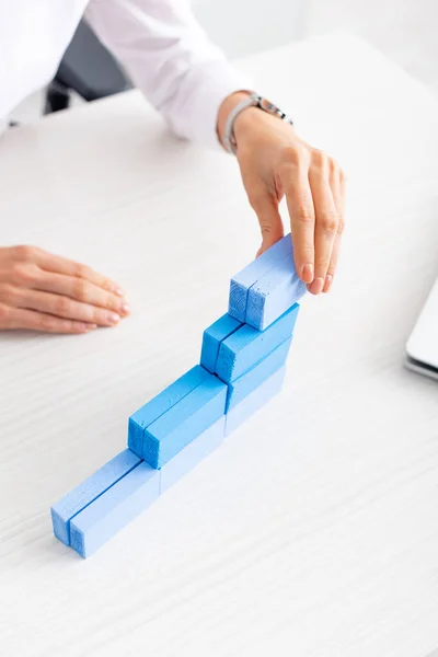 Cropped view of businesswoman stacking blue building blocks near laptop on table — Stock Photo