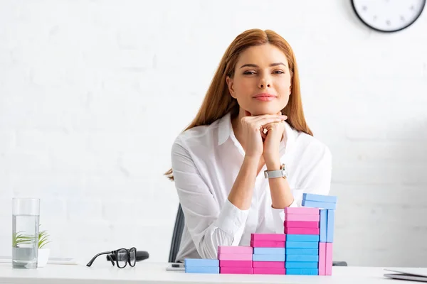 Attraktive Geschäftsfrau blickt von Bausteinen auf dem Tisch in die Kamera in der Nähe der Marketingpyramide — Stockfoto