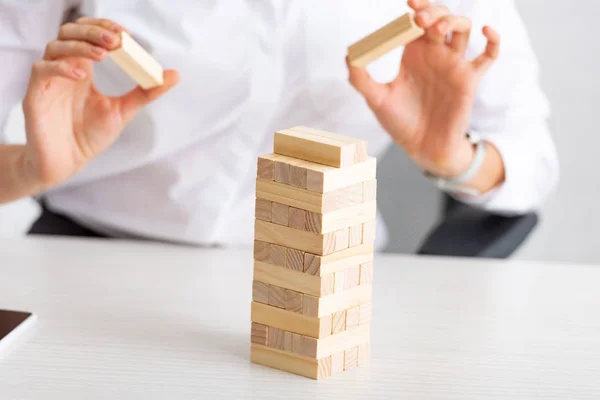 Ausgeschnittene Ansicht einer Geschäftsfrau, die Holzbausteine auf einem Tisch auf grauem Hintergrund stapelt — Stockfoto