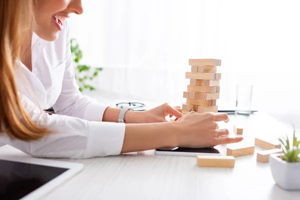 Vista recortada de una mujer de negocios sonriente apilando bloques de construcción de madera en la mesa - foto de stock