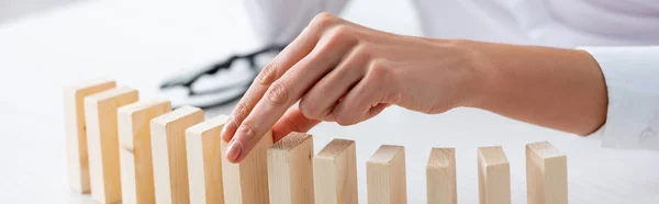 Vue recadrée d'une femme d'affaires tenant un bloc de construction en bois à une table isolée sur une photo panoramique grise — Photo de stock