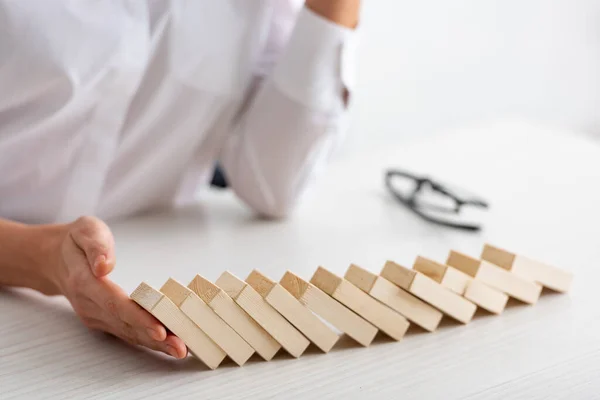 Vista recortada de la mujer de negocios sosteniendo bloques de construcción que caen sobre la mesa sobre fondo blanco - foto de stock