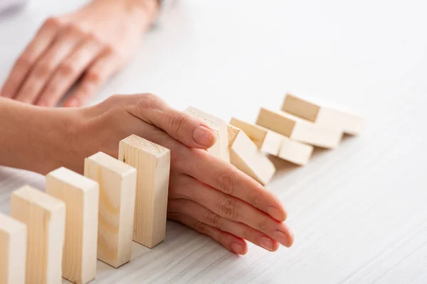 Cultivado con de mujer de negocios sosteniendo bloques de construcción que caen con la mano en la mesa sobre fondo blanco - foto de stock