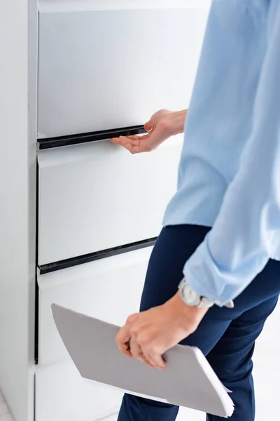 Cropped view of businesswoman with paper folder opening cabinet driver isolated on white — Stock Photo