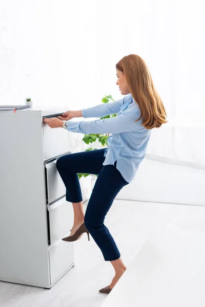 Vista lateral de la mujer de negocios tratando de abrir el conductor del gabinete en la oficina - foto de stock