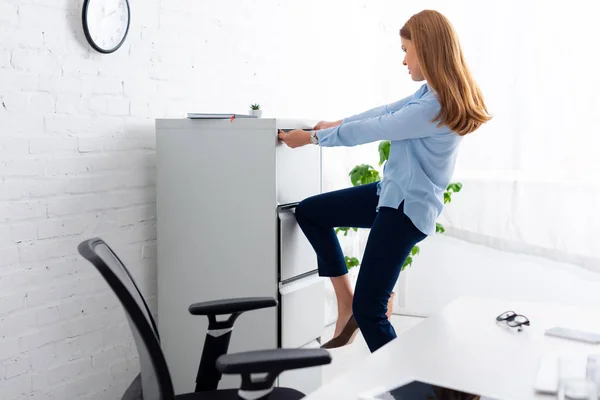 Side view of businesswoman trying to opening cabinet driver near table in office — Stock Photo