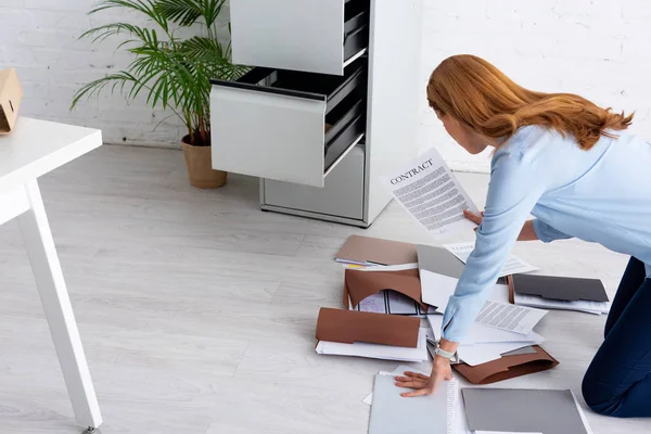 Vista lateral de la mujer de negocios con contrato cerca de documentos en el piso en la oficina - foto de stock