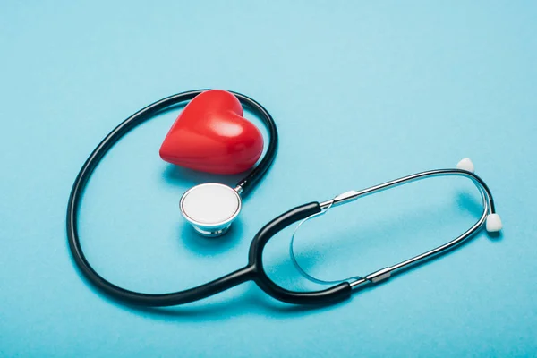 Corazón rojo decorativo y estetoscopio sobre fondo azul, concepto del día mundial de la salud - foto de stock