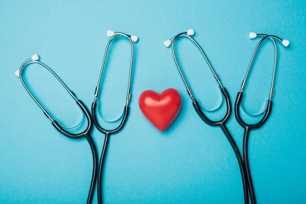 Draufsicht auf dekoratives rotes Herz mit Stethoskopen auf blauem Hintergrund, Konzept zum Weltgesundheitstag — Stockfoto