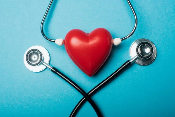 Вид зверху на декоративне серце зі стетоскопами на синьому фоні, концепція Всесвітнього дня здоров'я — стокове фото