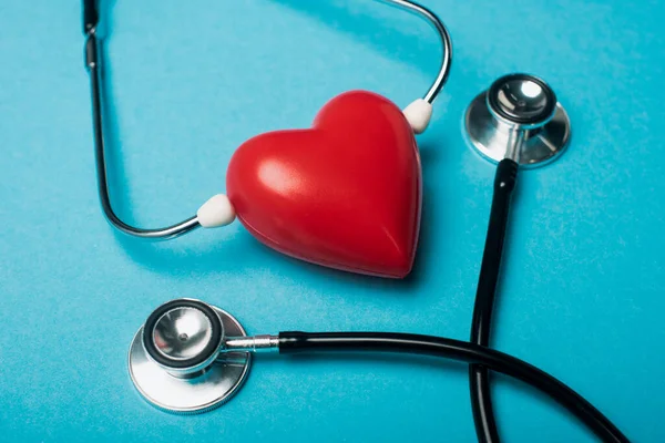 Corazón rojo decorativo y estetoscopio negro sobre fondo azul, concepto del día mundial de la salud - foto de stock