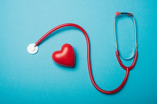 Vista superior del corazón decorativo junto al estetoscopio rojo sobre fondo azul, concepto del día mundial de la salud - foto de stock