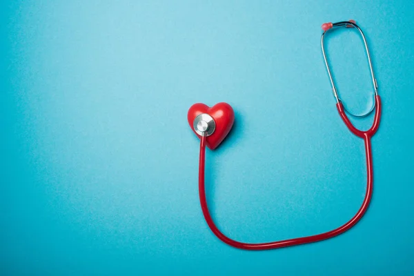 Vue du dessus du coeur décoratif relié au stéthoscope rouge sur fond bleu, concept de journée mondiale de la santé — Photo de stock