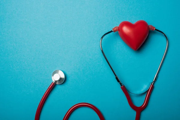 Vue du dessus du stéthoscope relié au coeur rouge décoratif sur fond bleu, concept de journée mondiale de la santé — Photo de stock