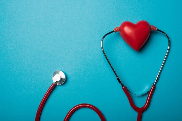 Vista superior del estetoscopio conectado con el corazón rojo decorativo sobre fondo azul, concepto del día mundial de la salud - foto de stock