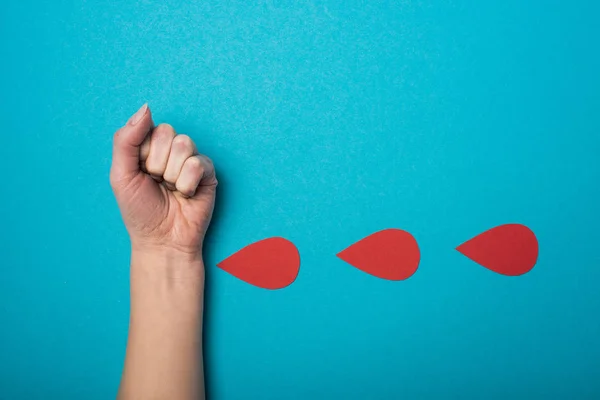 Vista superior de la imitación de gotas de sangre de la mano de la mujer sobre fondo azul, concepto del día mundial de la salud - foto de stock