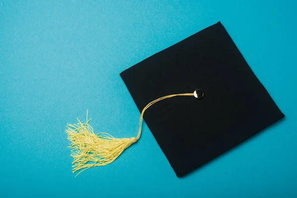 Schwarze Graduiertenmütze mit Quaste auf blauem Hintergrund — Stockfoto