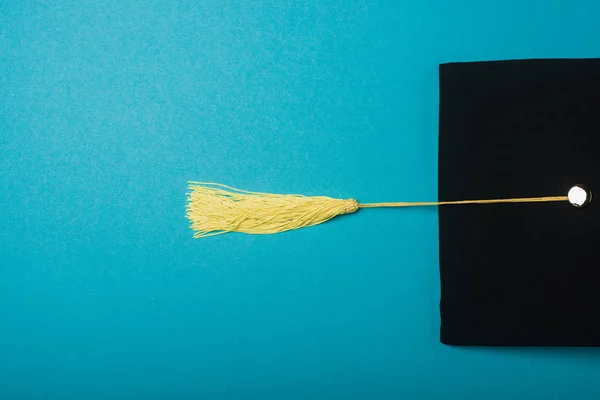 Top view of black graduation cap with yellow tassel on blue background — Stock Photo