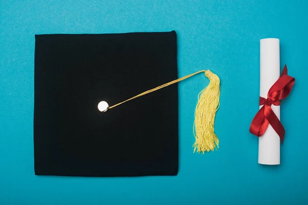 Vue du dessus du bonnet de graduation noir avec pompon jaune et diplôme sur fond bleu — Photo de stock