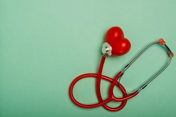 Вид сверху красного стетоскопа, связанного с декоративным сердцем на зеленом фоне, концепция Всемирного дня здоровья — стоковое фото