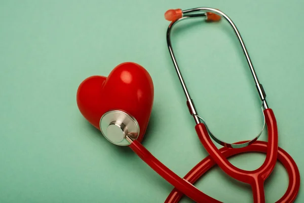 Estetoscopio rojo conectado con el corazón decorativo sobre fondo verde, concepto del día mundial de la salud - foto de stock