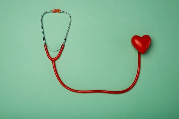 Вид сверху стетоскопа и декоративного красного сердца на зеленом фоне, концепция Всемирного дня здоровья — стоковое фото
