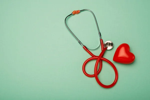 Vue du dessus du stéthoscope à côté du coeur rouge sur fond vert, concept de journée mondiale de la santé — Photo de stock