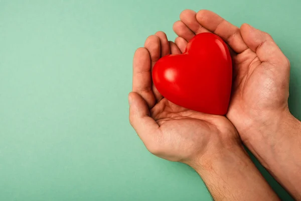 Vista cortada de coração vermelho decorativo em mãos de homem no fundo verde, conceito de dia de saúde mundial — Fotografia de Stock