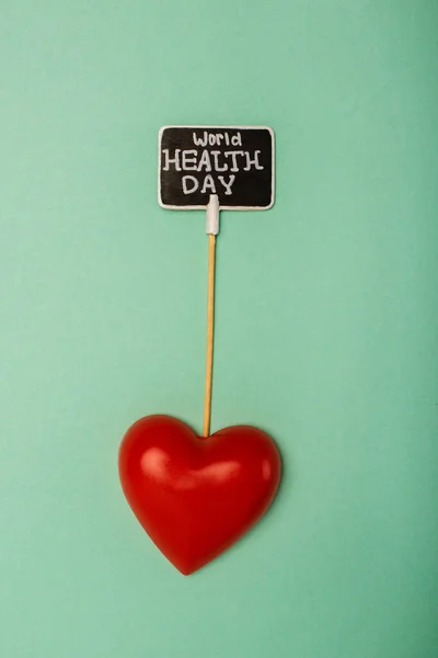 Вид зверху на декоративне червоне серце і листівки зі світовим днем здоров'я на зеленому фоні — стокове фото
