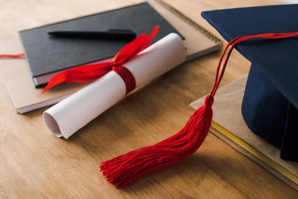 Selektive Fokussierung von Notizbüchern, Stift, Diplom und Abschlussmütze mit roter Quaste auf Holzgrund — Stockfoto