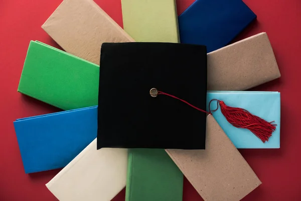 Vue du dessus de la casquette de graduation noire avec pompon sur des livres sur fond rouge — Photo de stock
