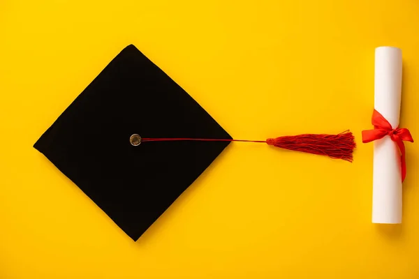 Vista superior do diploma e tampa de graduação com borla vermelha no fundo amarelo — Fotografia de Stock