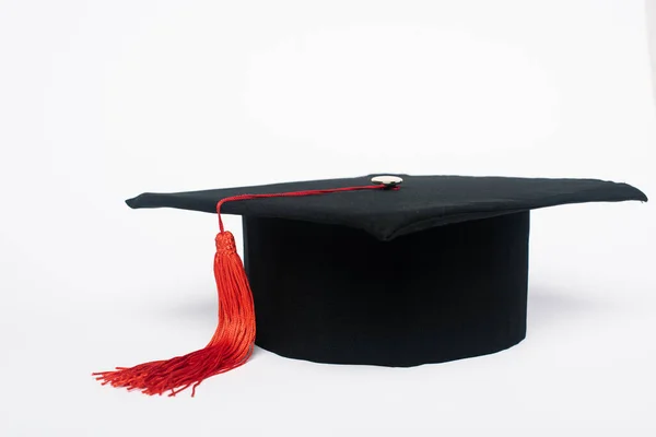 Black graduation cap with red tassel on white background — Stock Photo